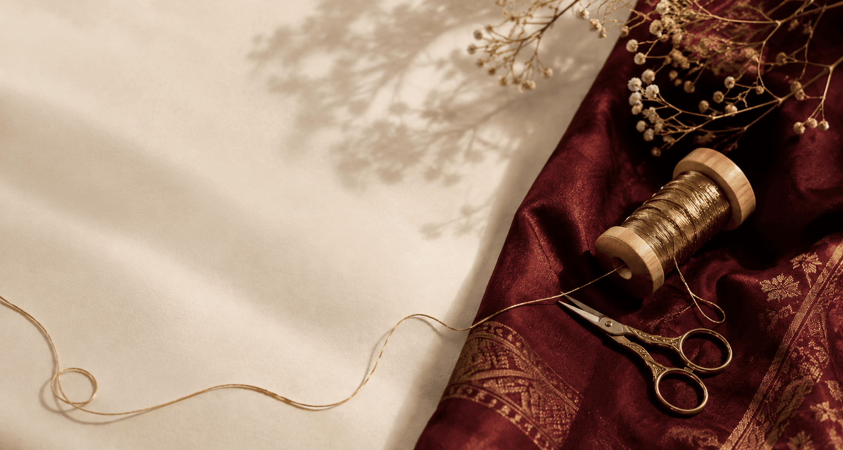 Scissors and gold thread beside maroon silk fabric