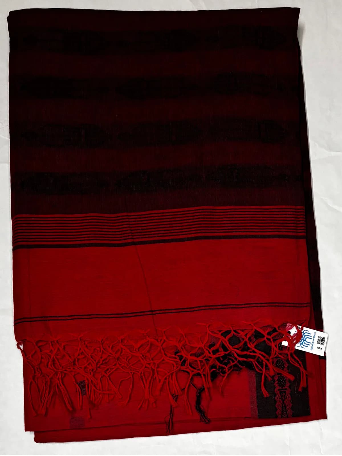 Folded Tilottama red and black handloom saree showcasing contrasting borders and tassels